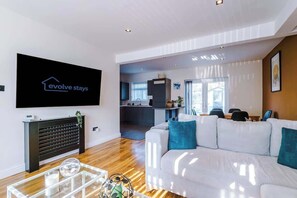 A modern living room with a sofa, a coffee table, and a TV mounted on the wall displaying 'evolve stays'.