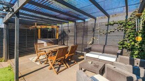 A covered patio with a table and chairs, a sofa, and a grill area. - Game Room | Summer House | 3Bed Home In Stretford (Manchester)