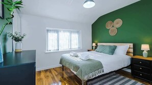 A bedroom with a bed, bedside tables, a window, a green wall, and a plant. - Game Room | Summer House | 3Bed Home In Stretford (Manchester)