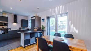 A modern kitchen with a dining area, built-in appliances, and a large window. - Game Room | Summer House | 3Bed Home In Stretford (Manchester)