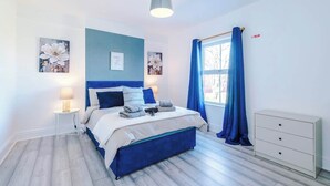 Un dormitorio con cama, lámparas de noche, cómoda y ventana con cortinas.