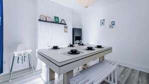 Un comedor con una mesa blanca dispuesta para cuatro personas, una silla blanca, un banco blanco y una pared blanca con una estantería.