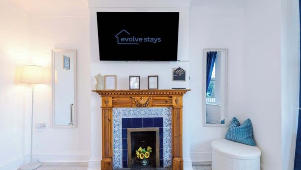 Una sala de estar moderna con chimenea, un televisor montado que muestra 'evolve stays' y un pequeño rincón de descanso.