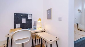 Ein Zimmer mit Schreibtisch, Stuhl, Bett und einer Pinwand mit Papieren.