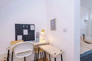 Ein Zimmer mit Schreibtisch, Stuhl, Bett und einer Pinwand mit Papieren.