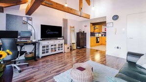 Un salon moderne avec un plafond en bois, un téléviseur à écran plat, un bureau avec un ordinateur, un canapé et un fauteuil en osier.