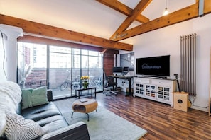 A modern living room with a sofa, a television, and a dining area with a table and chairs. - Central MCR 2BR/2BA • Workspace • Full Kitchen (Manchester)