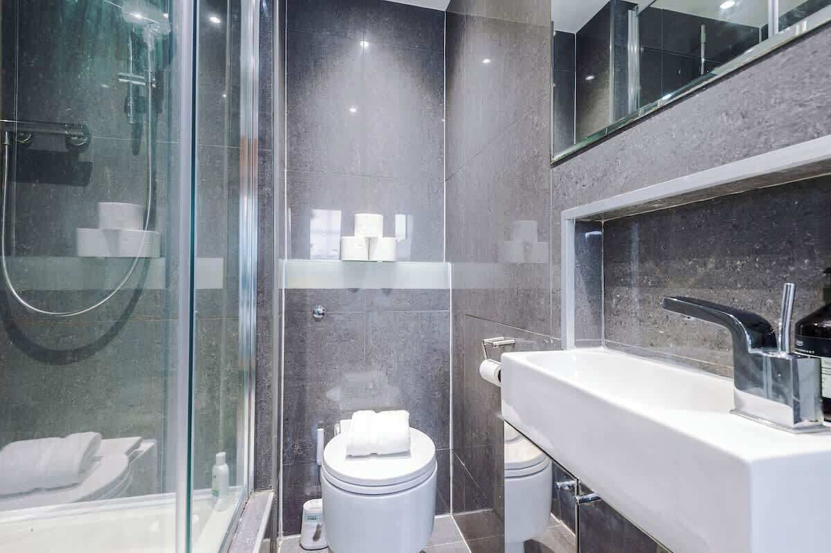 A modern bathroom with a glass-enclosed shower, a white sink with a chrome faucet, and a toilet with a white lid.
