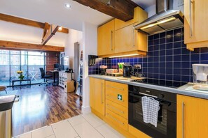 A modern kitchen with wooden cabinets, a black oven, and a blue tiled backsplash. - Central MCR 2BR/2BA • Workspace • Full Kitchen (Manchester)