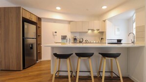 Una cocina moderna con refrigerador empotrado, armarios de madera, encimera blanca y tres taburetes negros.