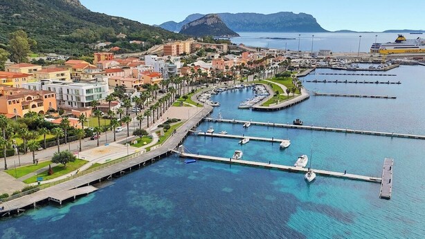 Una cittadina costiera con un porto turistico, acque blu cristalline e edifici lungo la passeggiata.