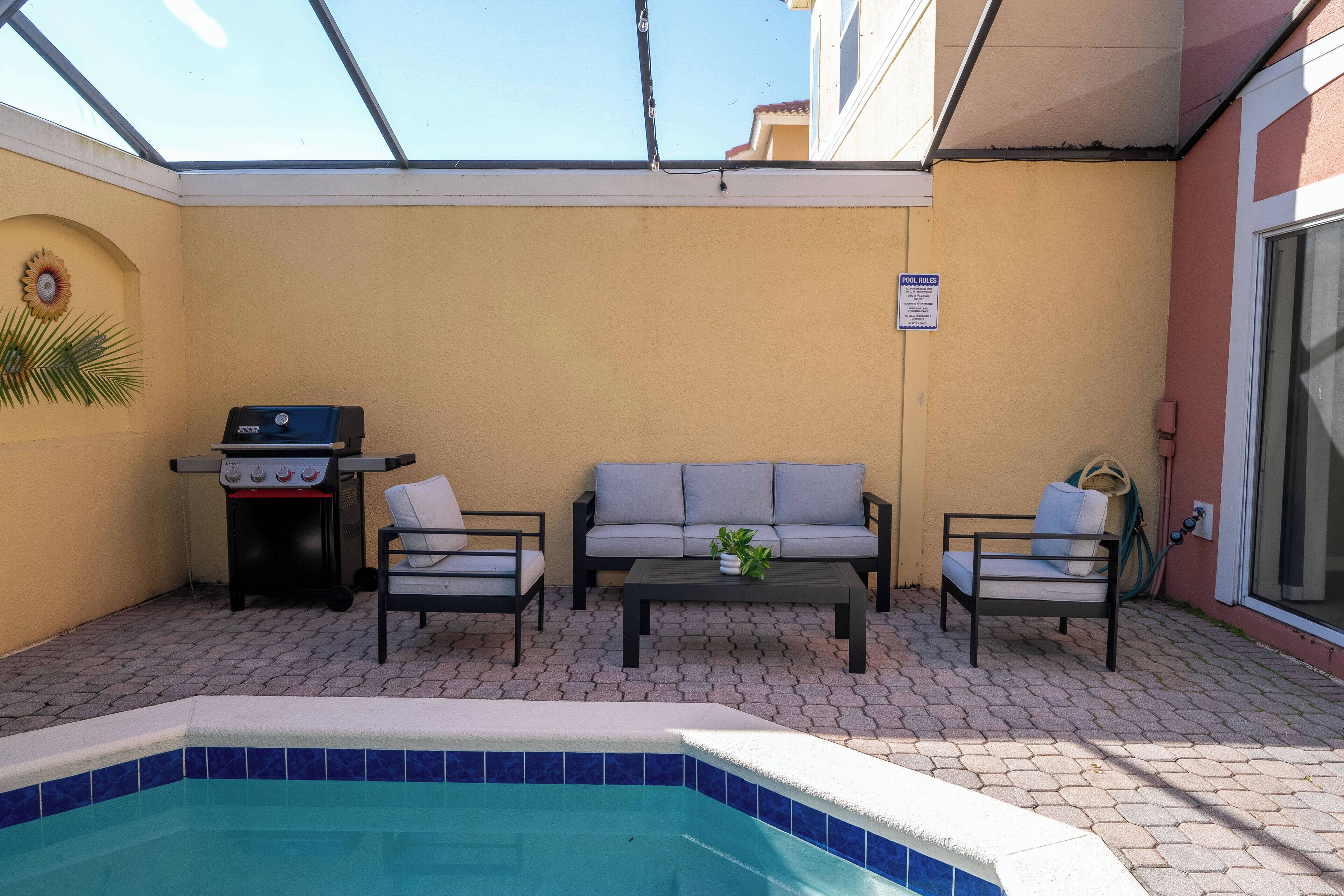 Une terrasse extérieure avec une piscine, un barbecue et deux canapés.