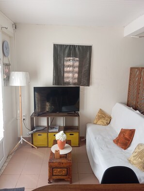 Ein Wohnzimmer mit Fernseher auf einem Holzschrank, einem kleinen Tisch mit einer Vase und einer Couch mit Kissen.