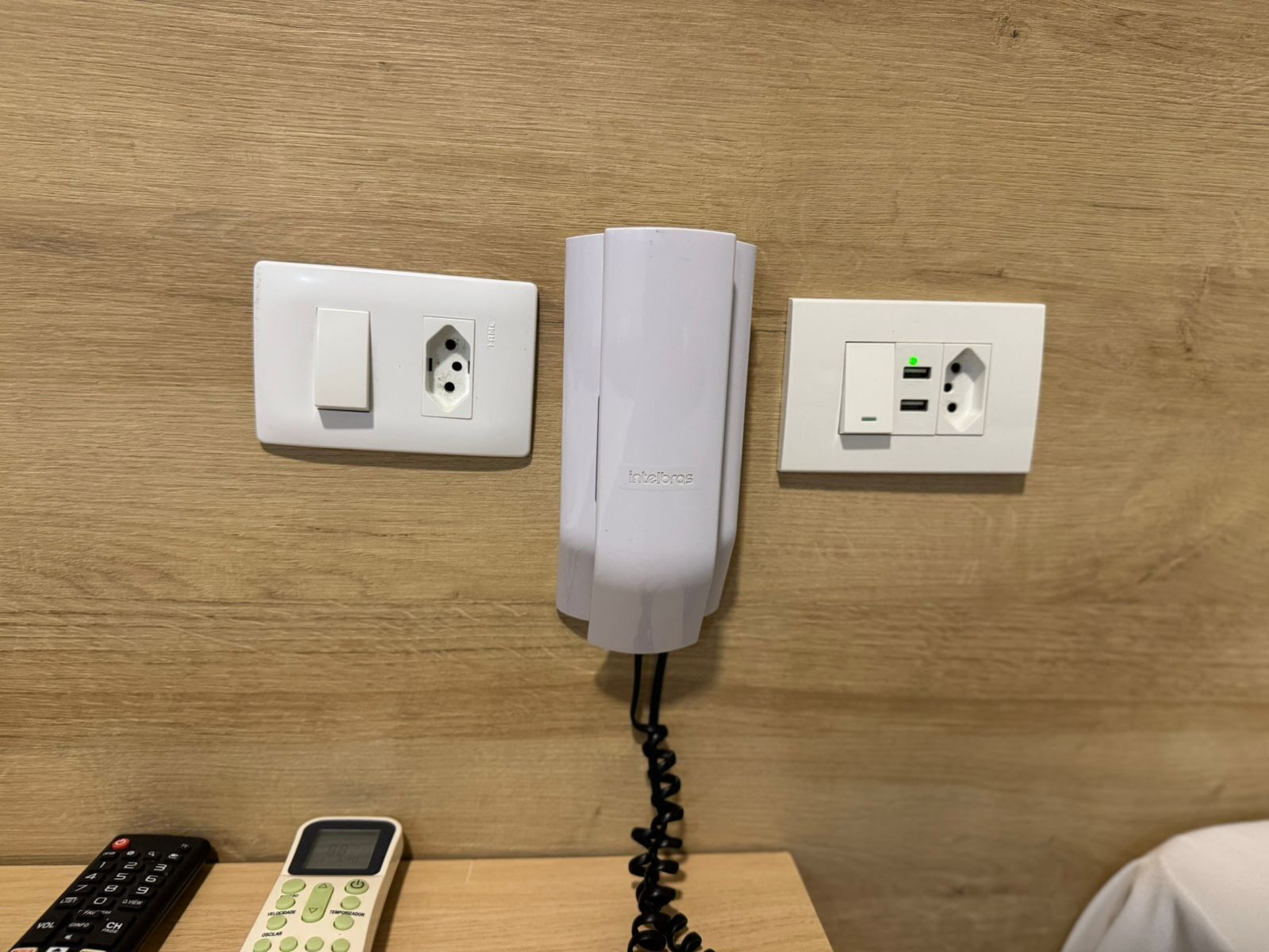 Un telefono fissato al muro, una presa di corrente e una porta USB per la ricarica su una superficie in legno.