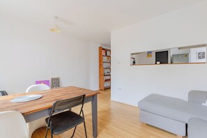 Un espai modern d'estar amb zona de menjador, un sofà gris i una biblioteca de fusta.