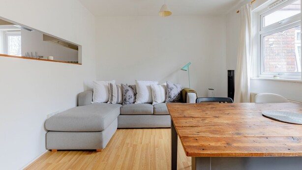 Een moderne woonkamer met een grijze modulaire bank, een houten eettafel en een hanglamp.