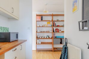 Eine kleine Küche mit Mikrowelle, Holzschränken und einem Bücherregal mit verschiedenen Gegenständen.