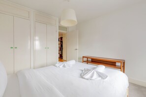 A neatly made bed with white linens and towels, a wooden bedside table, and a wardrobe with a mirror. - Well Connected 1BDR Flat in the Heart of Islington (Greater London)