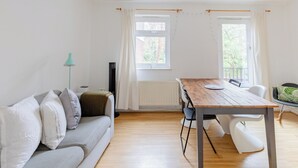 Een moderne woonkamer met een houten eettafel, een grijze bank en een raam met gordijnen.