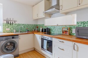 Een compacte keuken met een wasmachine, oven, magnetron en een betegelde spatwand.