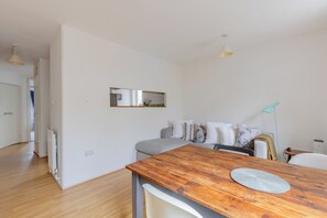 Een moderne, minimalistische woonruimte met een houten eettafel, een zithoek en een klein keukenhoekje.