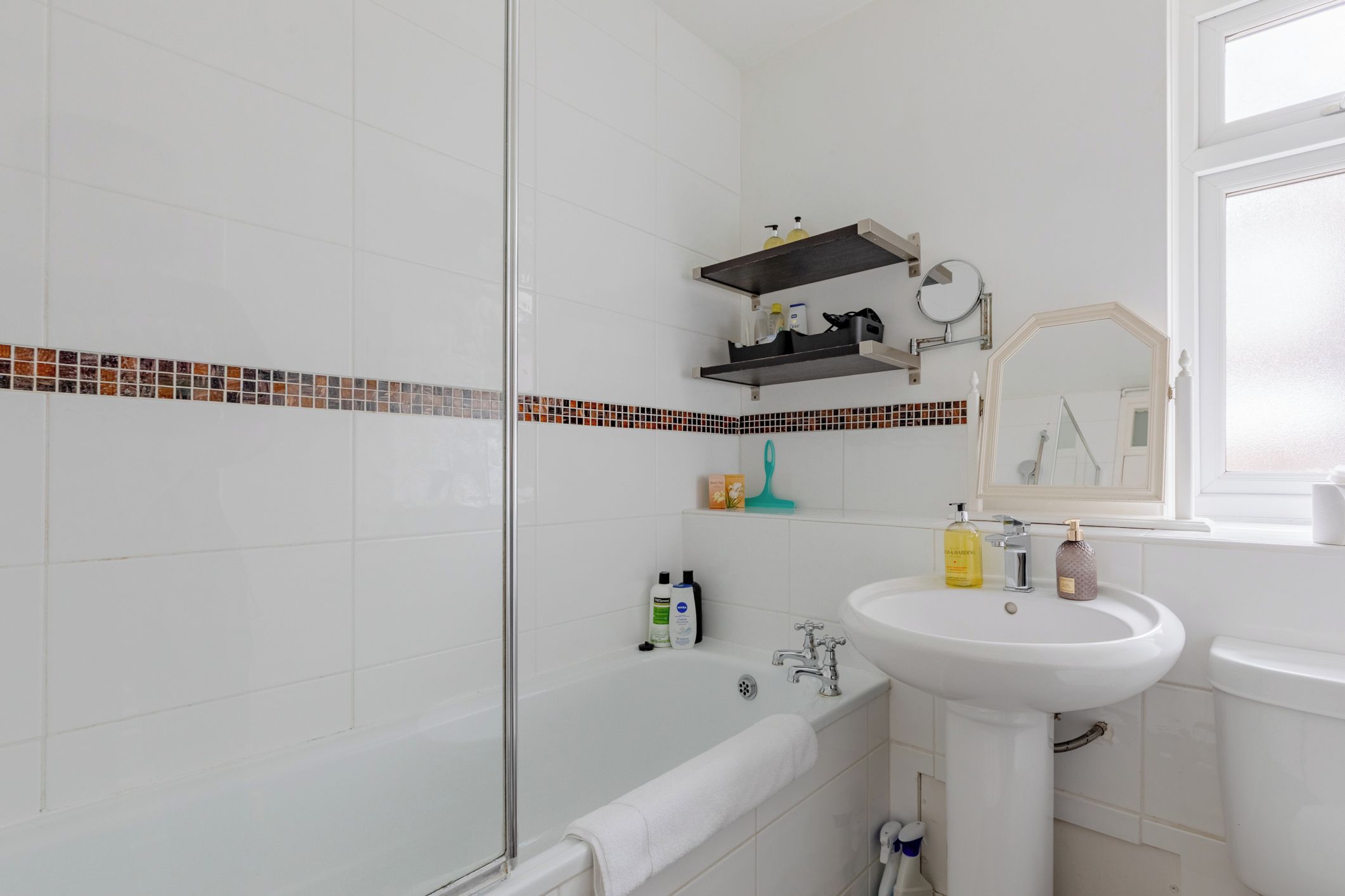 A bathroom with a white sink, a mirror, a shower, and a toilet. There are toiletries on the sink and a towel on the floor.