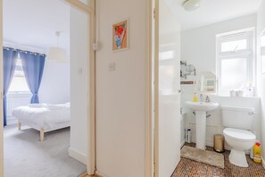 Ein Zimmer mit einem Bett sowie ein Badezimmer mit Toilette, Waschbecken und Spiegel.