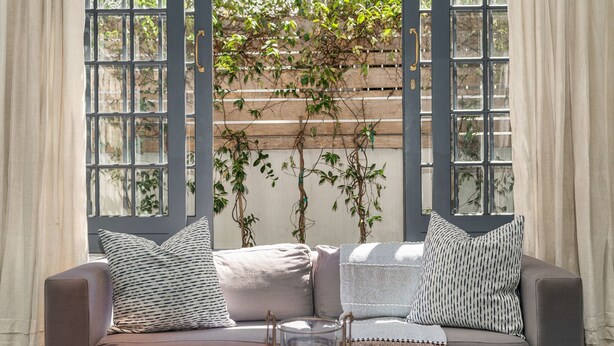 A cozy seating area with a cushioned sofa, a glass candle holder, and a view of a wooden trellis with climbing plants. - Bellevue House - Three Bedroom House, Sleeps 6 (Cape Town)