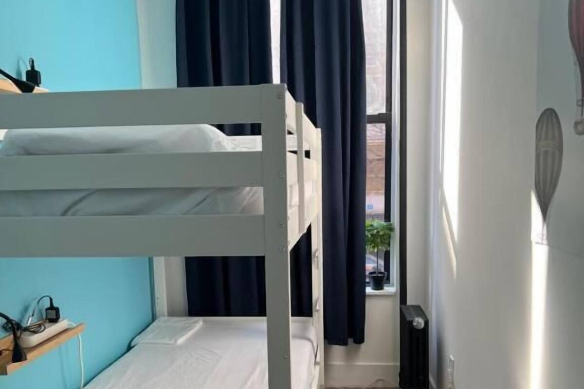A bunk bed room with a window, curtains, and a small shelf with items.