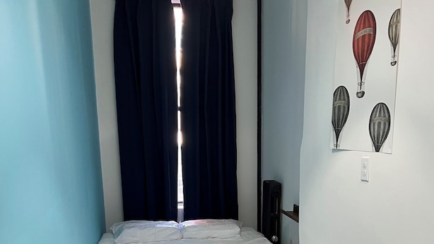 A small, neatly made room with a bed, a chair, a lamp, and a wall with hot air balloon artwork. - East Harlem Hostel (New York)