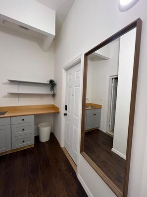 A small, clean bathroom with a wooden vanity, a mirror, and a white door. - East Harlem Hostel (New York)