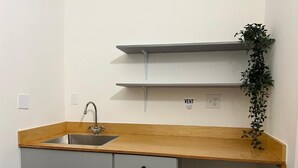 A kitchen with a sink, wooden countertop, grey cabinets, and a plant on a shelf. - East Harlem Hostel (New York)
