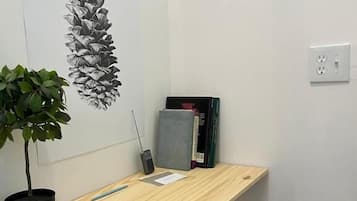 A small, neatly organized office space with a wooden desk, a potted plant, a red chair, and a wall-mounted shelf with books and a phone.