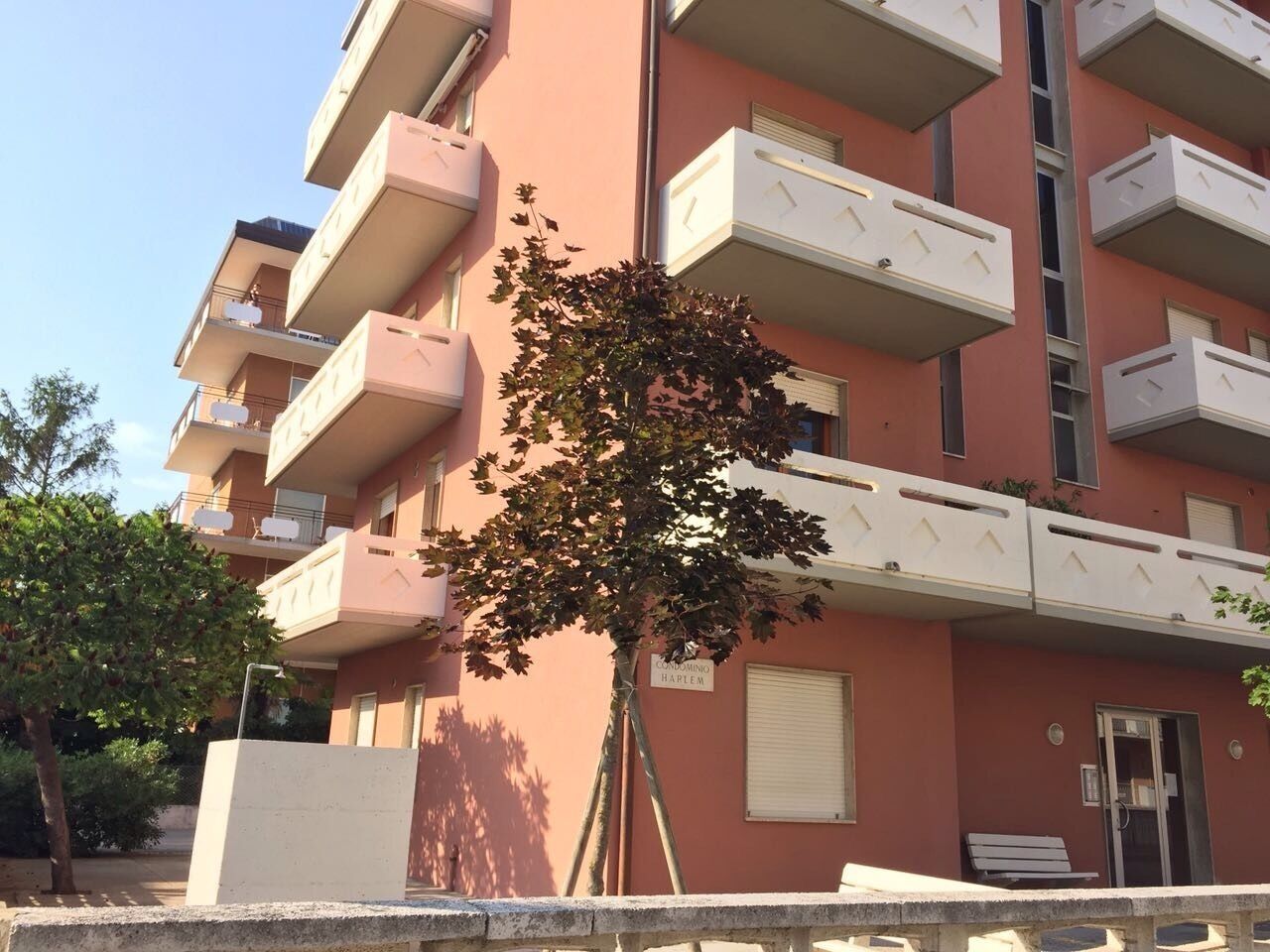 A multi-story residential building with balconies, a tree in front, and a sign indicating it is a condominium.