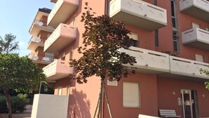 A multi-story residential building with balconies, a tree in front, and a sign indicating it is a condominium. - APARTMENT IN THE SUN OF JESOLO (Lido di Jesolo)