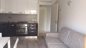 A modern kitchen with white cabinets, a stove, and a dining area with a white table and chairs. - APARTMENT IN THE SUN OF JESOLO (Lido di Jesolo)