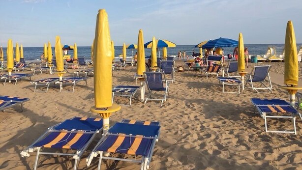 A beach with rows of sun loungers and umbrellas, some with blue and yellow colors. - APARTMENT IN THE SUN OF JESOLO (Lido di Jesolo)