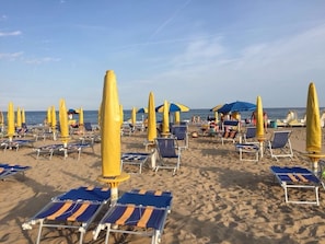 En strand med rader av solstolar och parasoller, vissa i blått och gult.