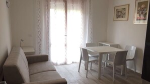 A living room with a sofa, a dining table with chairs, and a TV. - APARTMENT IN THE SUN OF JESOLO (Lido di Jesolo)
