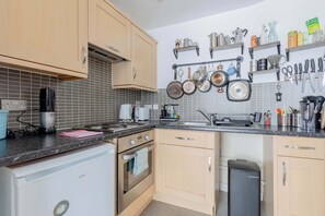 A kitchen with wooden cabinets, a built-in oven, a sink, and various kitchen utensils and appliances. - Bright and Trendy 1BD Canalside Flat in Hackney (Greater London)