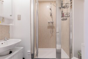 Une salle de bain moderne avec une douche à parois de verre, un lavabo blanc et des murs recouverts de carreaux beiges.