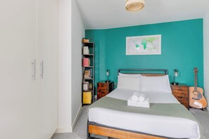A bedroom with a bed, a guitar, a bookshelf, and a map on the wall. - Bright and Trendy 1BD Canalside Flat in Hackney (Greater London)