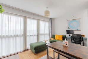 A modern living room with a green sofa, a wooden table, a black office chair, a small round table, a lamp, and a globe map on the wall. - Bright and Trendy 1BD Canalside Flat in Hackney (Greater London)