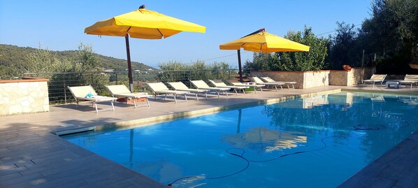 Une piscine entourée de murs de pierre et de verdure, avec des chaises longues et des parasols jaunes.