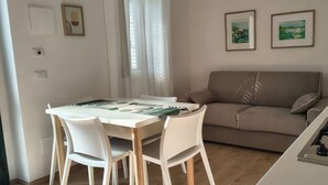 A compact living space with a dining table, chairs, a sofa, a kitchen area with a stove, and two framed pictures on the wall. - Panoramic apartment with pool 2 - Liberato Puglia (Peschici)