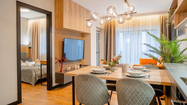 Een moderne hotelkamer met een zithoek, een aan de muur bevestigde televisie en een groot raam met gordijnen.