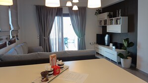 Ein modernes Wohnzimmer mit einer Couch, einem Esstisch mit einer Snackplatte, einem Fernseher und einem Bücherregal.
