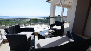 Ein Balkon mit Korbmöbeln, einem Glastisch und Blick aufs Meer.