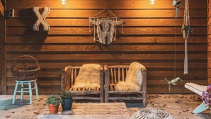 A rustic wooden cabin interior with a wooden bench, a woven basket, a small table, and a hanging macrame decoration.