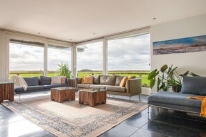 A spacious living room with a large window, a sofa set, a coffee table, and a rug. - 10P 4B Villa with Pool and Sauna in Spijkerboor (Spijkerboor)